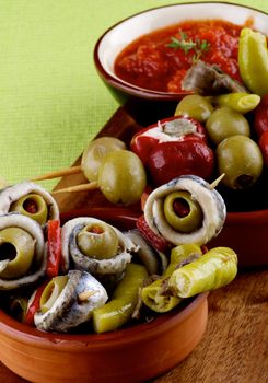 Delicious Spanish Snacks with Anchovies, Green Olives, Small Peppers Stuffed with Cheese and Tomatoes Sauce in Various Bowls closeup on Green Napkin. Focus on Foreground