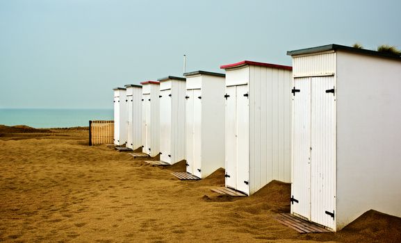 White Wooden Cabanas on Sand Beach in a Row on Blue Sky and Sea Edge Background Outdoors. French Atlantic Coast
