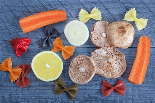 Raw mushrooms, vegetables, half of lemon and pasta on a blue wooden background.