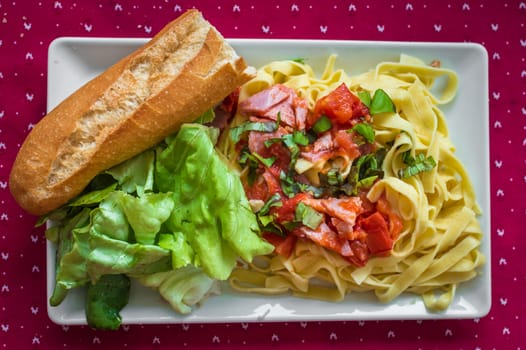 Salad with pasta, ham and vegetables in white plate on red tablecloth