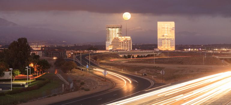Full moon over a California highway with headlight trails near at sunset.