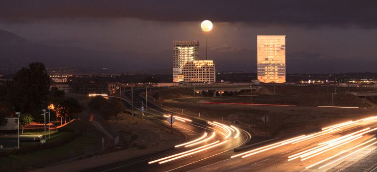 Full moon over a California highway with headlight trails near at sunset.