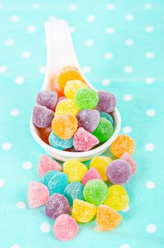 Colorful jelly candies in white spoon on tablecloth.