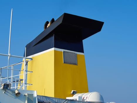 Black and yellow chimney of a cargo ferry ship with background of clear summer sky