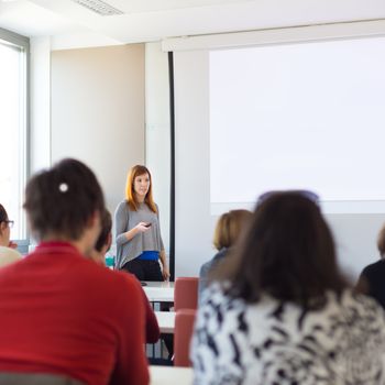 Speaker giving presentation in lecture hall at university. Participants listening to lecture and making notes. Copy space for brand on white screen.