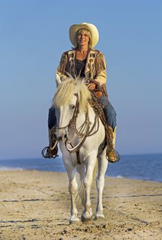 cowgirl on camargue horse on the beach