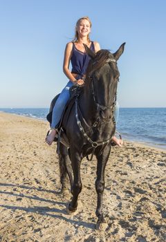 riding girl with her black stallion laughing on the beach