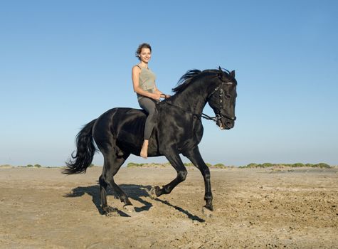 horse woman galloping with her black stallion on the beach