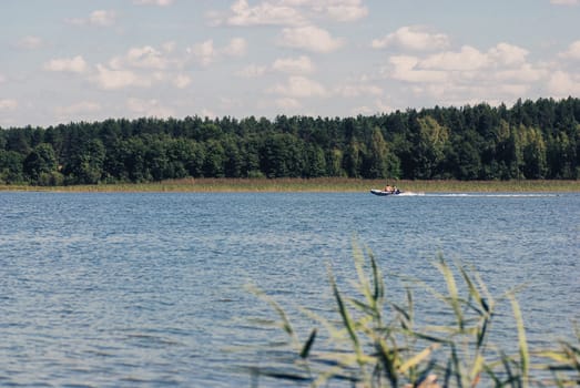 Lake and forest with running fishing boat at sunny day in Russia. Vacation.