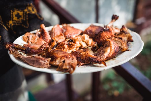 man's hand holds grilled roast chicken on white plate.