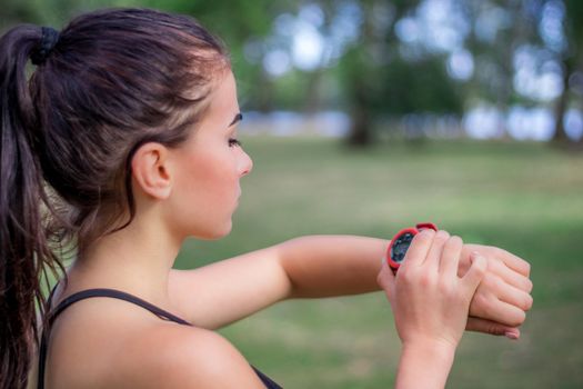 Young fitness girl checks stopwatch tracker on her wrist during running outdoor