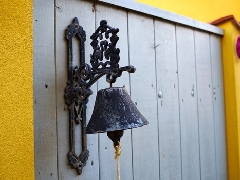 Close up view of an old vintage traditional metal bell hanging on a wooden fence door