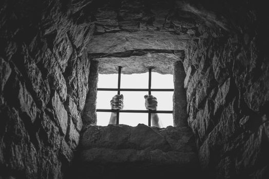 Freedom concept image, in monochrome settings, with a man holding the metal bars from a medieval german prison