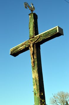 Cross of wooden crucifixion with a cock and under the blue sky.