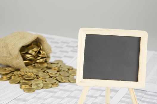 Close up empty blackboard on finance account have blur gold coins overflow from brown sack as background.