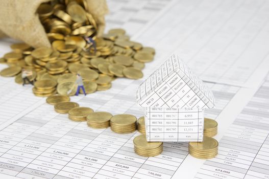 Close up house on pile of gold coins on finance account have blur gold coins overflow from brown sack with construction worker as background.