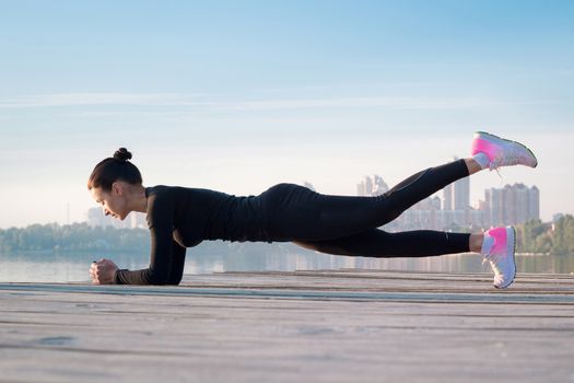 Young pretty fitness woman exercises on pier during morning sport training workout