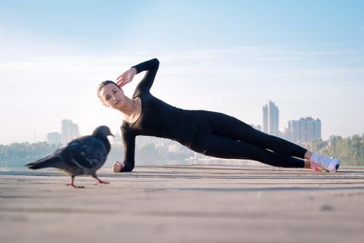 Young pretty fitness woman exercises on pier during morning sport training workout