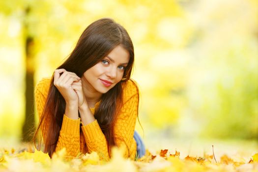 Young cute woman laying on dry leaves in autumn park