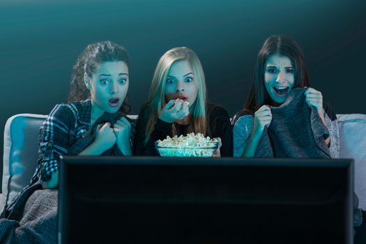 Teenage girls watching horror movie with popcorn