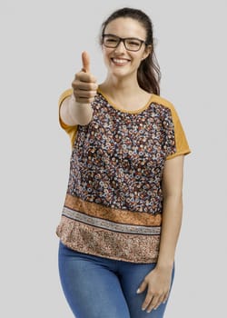 Studio portrait of a beautiful woman with thumbs up, isolated over a gray background 