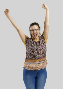 Beautiful and happy woman with both arms up, isolated over a gray background 