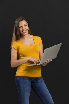 Beautiful woman in front of a black wall holding a laptop and pointing 