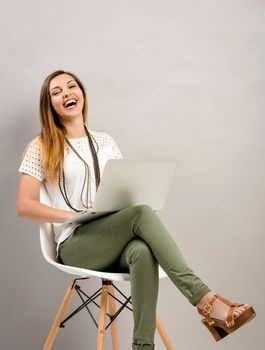 Beautiful young woman sitting on a chair with a laptop and laughing