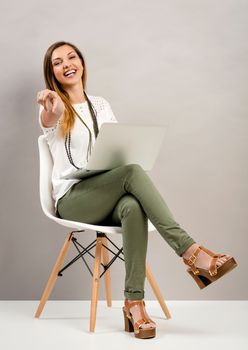 Beautiful woman sitting on a chair  with a laptop and pointing to the camera