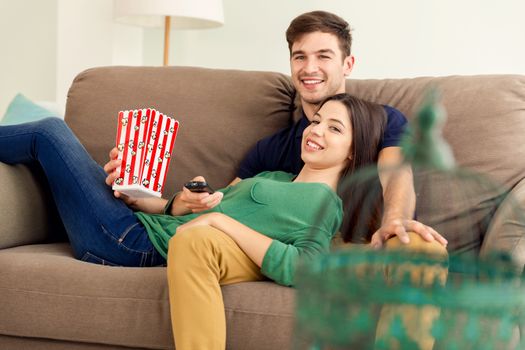 Young couple on the sofa and eating popcorns