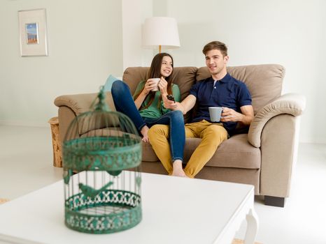 Young couple on the sofa drinking coffee while watching tv