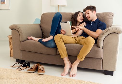 Young couple sitting on the sofa and watching something on a tablet