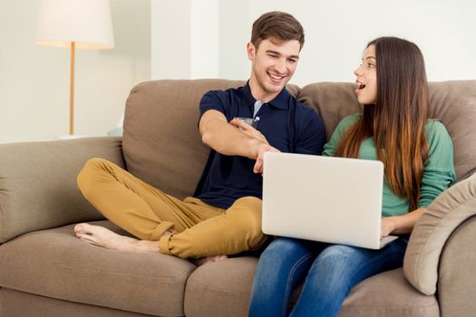 Young couple sitting on the sofa and watching something on a laptop