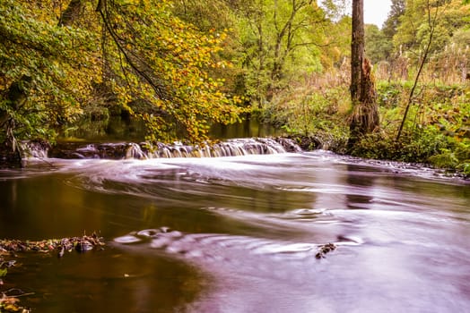 Mini waterfall in a forest in autumn on river Don In England