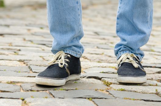 Feet dressed in blue jeans and sneakers man closeup on stone pavement