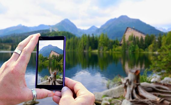 View over the mobile phone display during taking a picture of landscape in nature. Holding the mobile phone in hands and taking a photo. Focused on mobile phone screen.