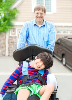 Caucasian father pushing disabled biracial  ten year old son in wheelchair outdoors. Child has cerebral palsy.
