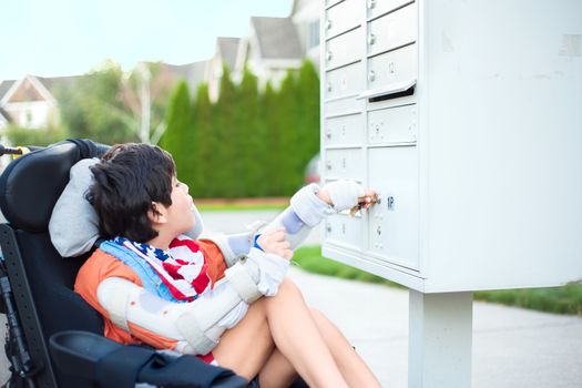 Disabled ten year old boy in wheelchair using key to open mailbox outdoors