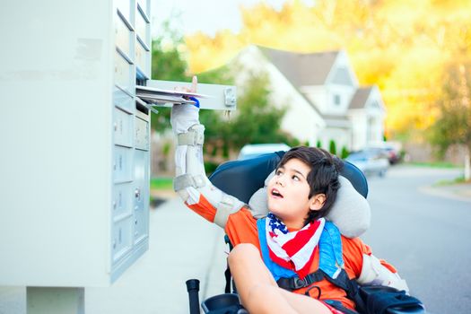 Disabled ten year old boy in wheelchair reaching up to get mail from mailbox outdoors