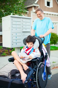 Disabled ten year old boy in wheelchair  getting mail from mailbox outdoors with father