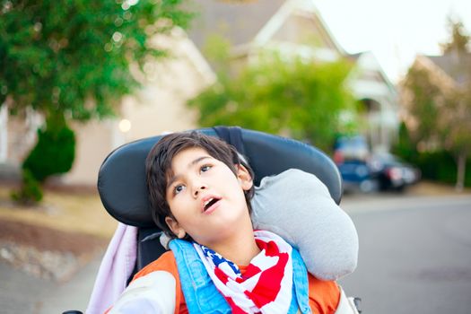Disabled ten year old boy sitting in wheelchair outdoors looking up into sky, thinking