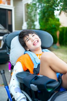 Biracial ten year old boy sitting in wheelchair outdoors smiling and relaxing