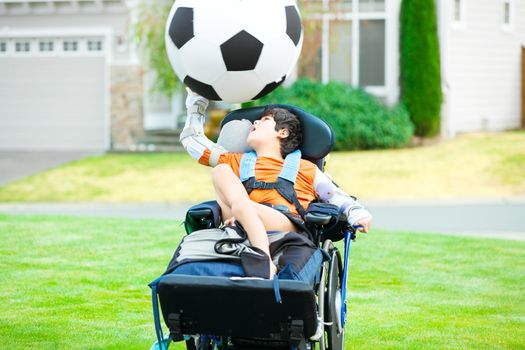 Ten year old biracial disabled boy in wheelchair playing with soccer ball at park