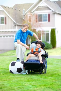 Caucasian father playing soccer with ten year old biracial disabled son in wheelchair at park outdoors
