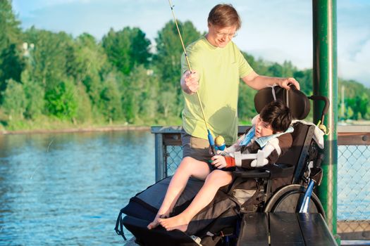 Caucasian father helping disabled ten year old son in wheelchair fish off pier