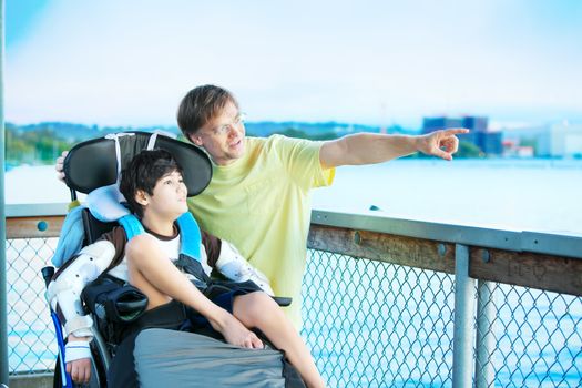 Caucasian father enjoying the lake with disabled ten year old son in wheelchair together