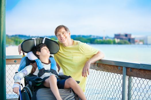 Caucasian father enjoying the lake with disabled ten year old son in wheelchair together