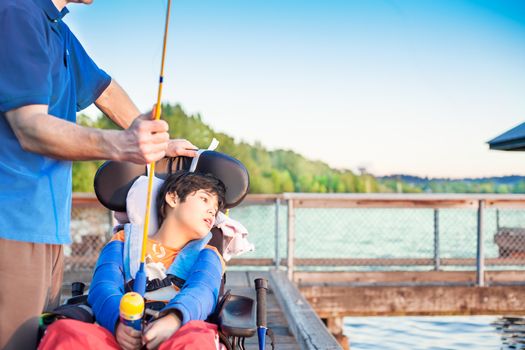 Caucasian father helping disabled ten year old son in wheelchair fish off pier