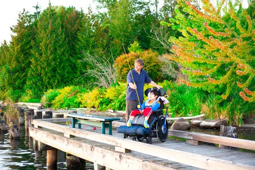 Caucasian father helping disabled ten year old son in wheelchair fish off pier