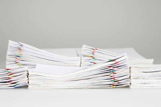 Pile overload document of receipt and report with colorful paperclip have blur pile paperwork as background on white table.